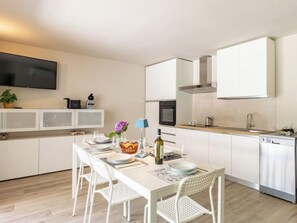 A modern kitchen with white cabinetry, a dining table set for four, and a flat-screen TV mounted above the counter. - Laghetto by Interhome (Colico)