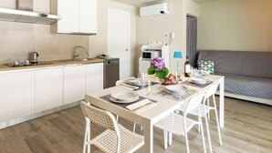 Een moderne keuken met witte kastjes, een eettafel voor vier personen en een grijze bank in de woonkamer.