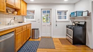 A compact kitchen with wooden cabinets, a stainless steel dishwasher, a sink with a faucet, a trash can, a stove, and a microwave. - Vineyard Views + Two Porches | Willow Creek AVA | Dunning Ranch Guest Suite Two (Paso Robles)