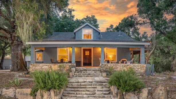 A two-story house with a stone staircase leading to the front door, surrounded by greenery and trees. - Vineyard Views + Two Porches | Willow Creek AVA | Dunning Ranch Guest Suite Two (Paso Robles)