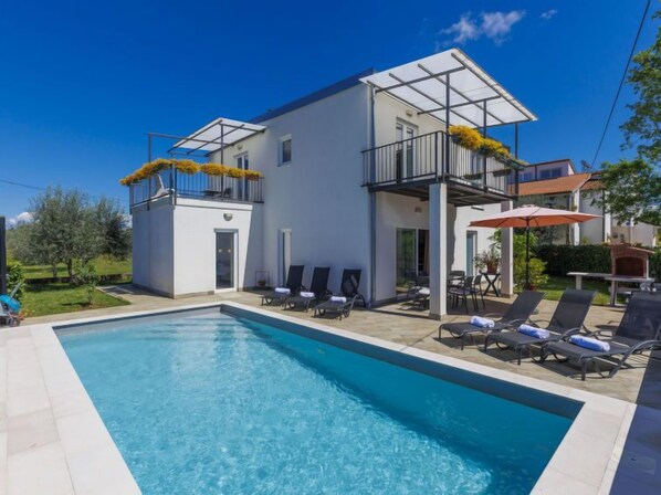 Un edificio moderno de dos pisos con piscina, zona de estar al aire libre y un patio cubierto.