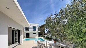 Et moderne hus med swimmingpool, udendørs møbler og et stort træ.