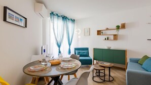 Een moderne woonkamer met een eethoek, met een ronde tafel met stoelen, een bank en een groene kast.
