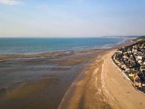 Vue aérienne d’une ville côtière, avec une longue plage de sable et un ensemble dense de bâtiments le long de la côte.