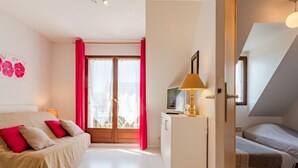 Une chambre à coucher avec un lit, un bureau, une télévision et une fenêtre avec des rideaux.