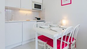 Une cuisine moderne avec des meubles blancs, un four à micro-ondes et une table à manger avec des chaises blanches et des coussins rouges.