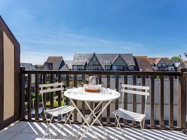 Un balcon avec une table ronde et deux chaises, donnant sur une rangée de maisons.