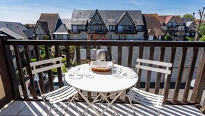 Un balcon avec une table ronde et des chaises blanches, donnant sur une rangée de maisons traditionnelles.