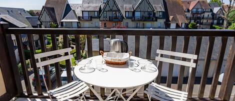 A balcony with a round table and white chairs, overlooking a row of traditional houses.