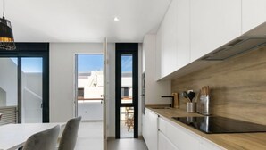 Une cuisine moderne avec des armoires blanches, un plan de travail en bois et une cuisinière noire. On aperçoit un coin repas avec une table et des chaises à travers une porte ouverte.