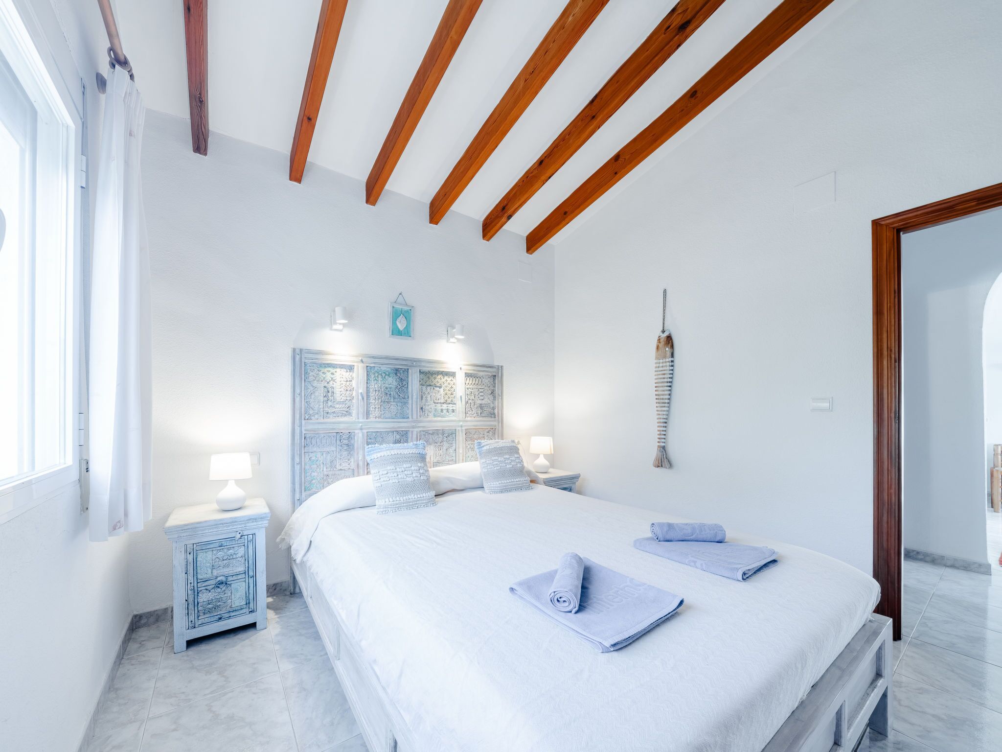 Une chambre avec un grand lit, deux tables de chevet, un plafond en bois et un élément décoratif mural.