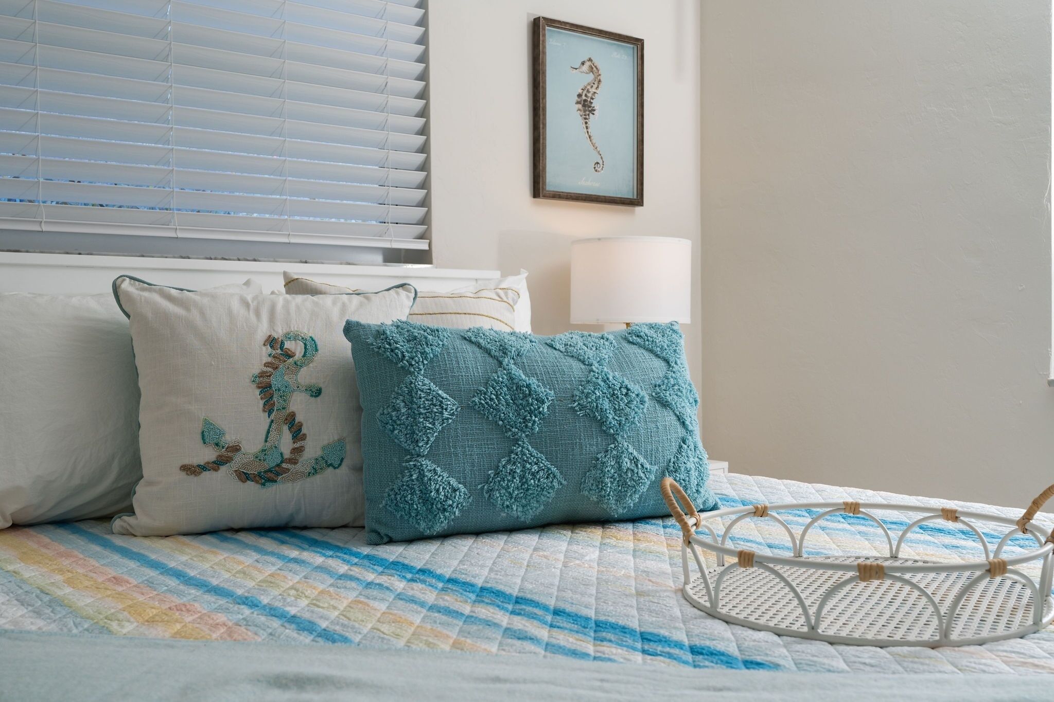 A bed with a quilt, two pillows, a bedside lamp, and a framed seahorse artwork on the wall.