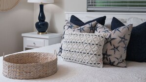 A bedroom with a bed, a bedside table with a lamp, a wall decoration, and a window with blinds. - 5027 Fairfield Dr - Paradise Palms 3 Bedroom Home by RedAwning (Fort Myers)