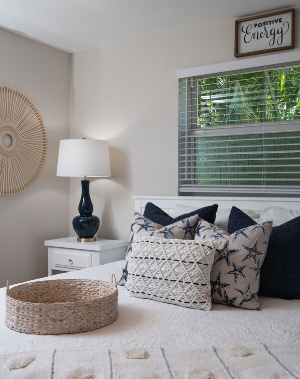 Un dormitorio con cama, mesita de noche con lámpara, decoración en la pared y ventana con persianas.