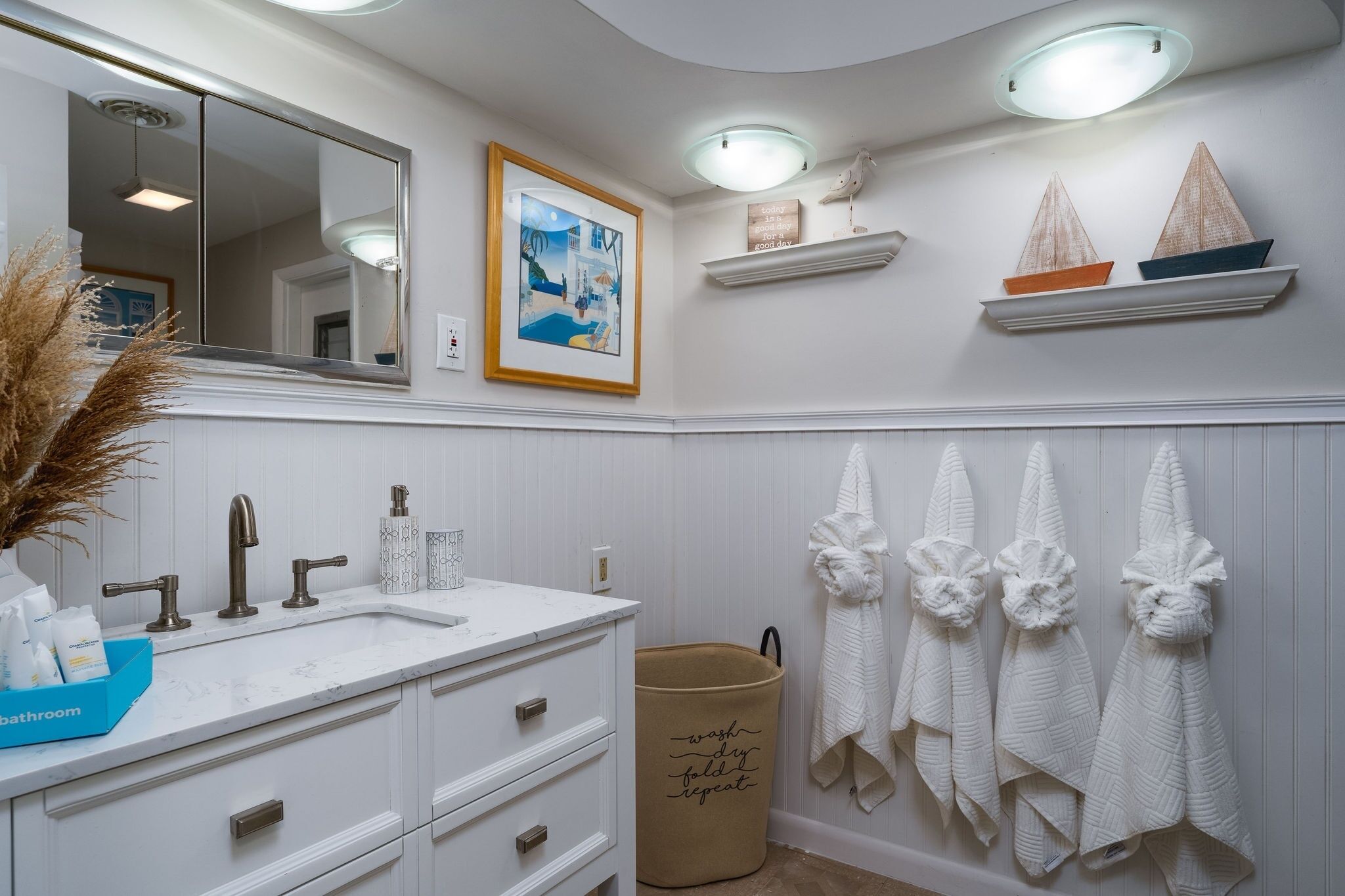 A bathroom with a white vanity, a large mirror, a framed picture, and decorative towels.