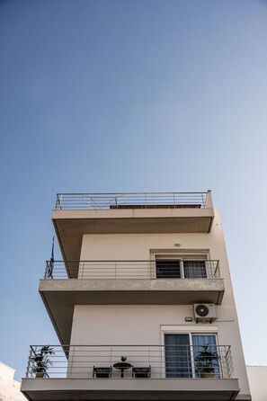 Un edificio de varios pisos con balcones, una ventana con cortina y un equipo de aire acondicionado.