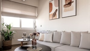A modern living room with a sofa, a coffee table, a potted plant, and artwork on the wall. - Vinnies Homes (Heraklion)