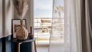 A room with a large window, a woven vase with pampas grass, and a framed artwork on a small table. - Vinnies Homes (Heraklion)