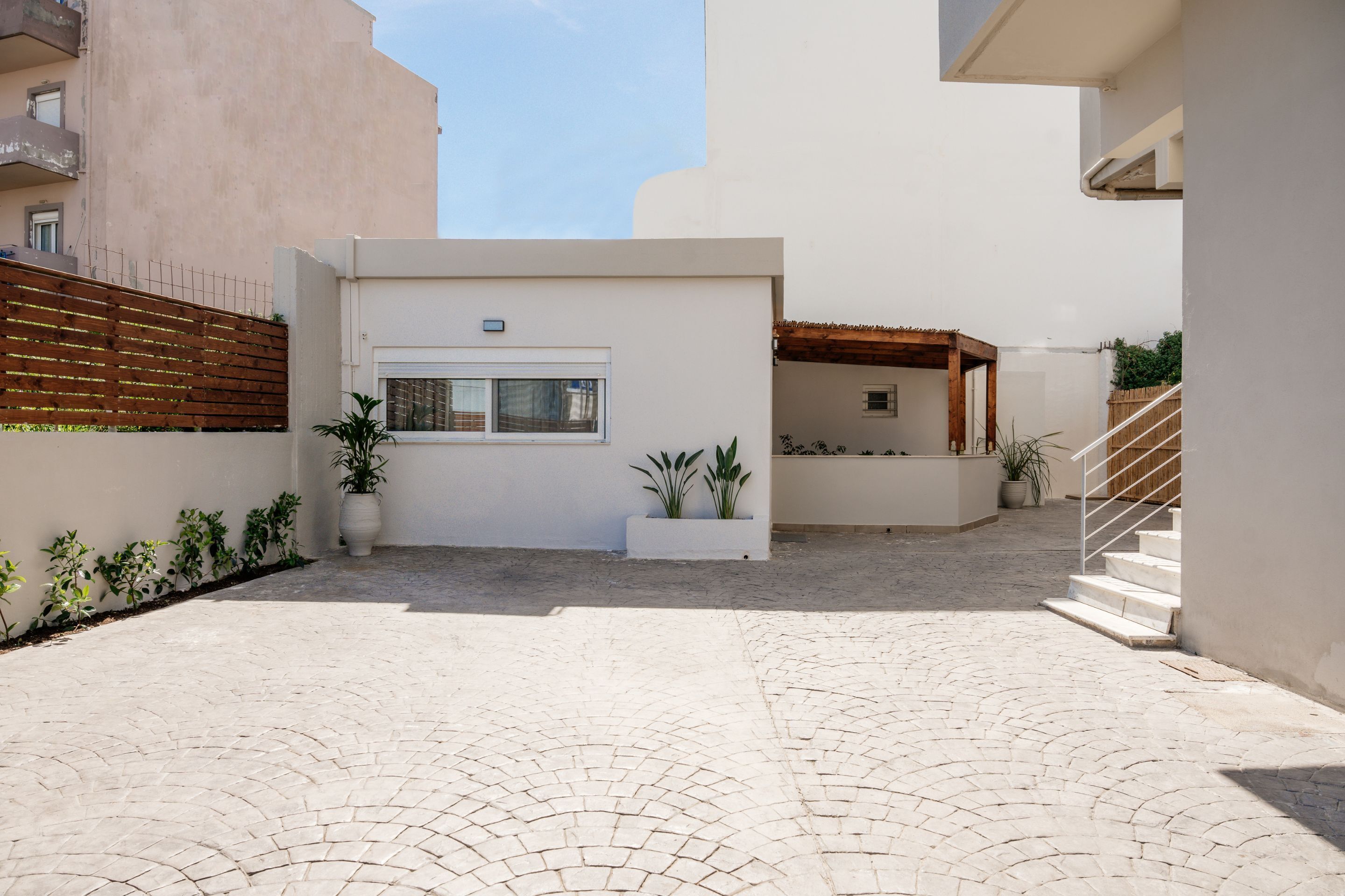 A courtyard with a paved floor, a white wall with a window, and a wooden fence.