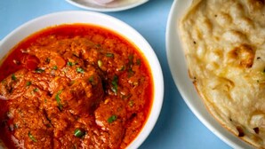 Un bol de curry accompagné de pain naan, le tout posé sur une table bleue.