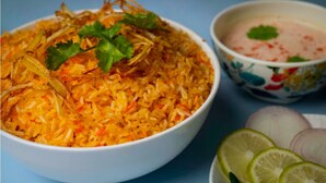 Un bol de riz garni de coriandre et d’oignons frits, accompagné d’un bol de sauce, d’oignons en tranches et de quartiers de citron vert.