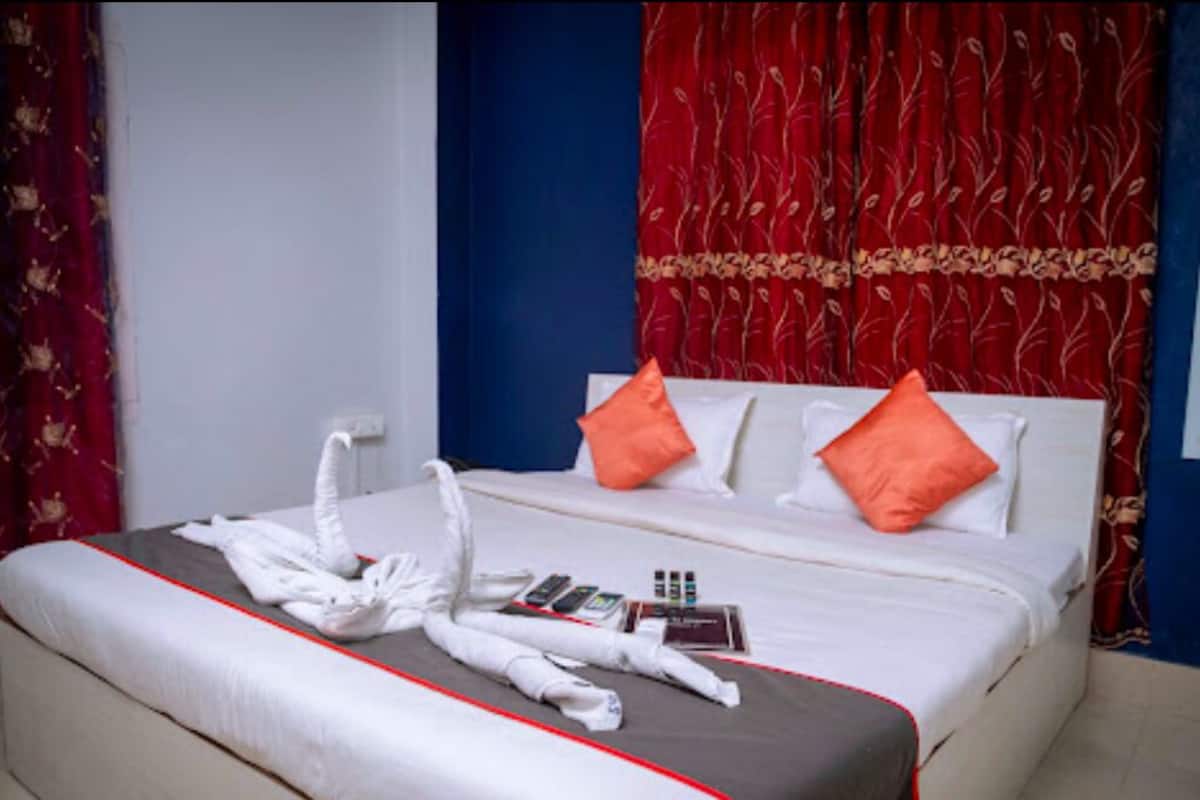 A neatly made bed with white bedding, two orange pillows, and a set of towels on the bed.