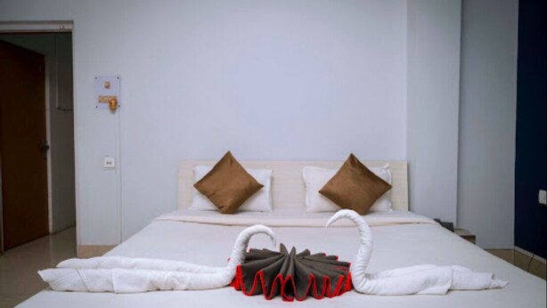 Une chambre d’hôtel avec un lit bien fait, deux oreillers, un interrupteur fixé au mur et une porte sur le côté gauche.