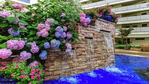 Un hôtel doté d’un mur en pierre, d’une fontaine à eau en cascade et d’une piscine à l’eau bleue.