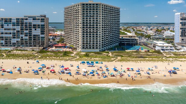 Un hôtel situé en bord de mer, avec plusieurs étages, une piscine et des parasols sur la plage.