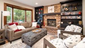 A living room with a fireplace, a bookshelf, and a large window.