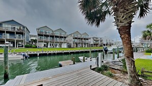 A waterfront property with a dock, a grassy area, and a building with multiple balconies. - Driftwood | Canal Front, Sound View, Private Dock! (Topsail Beach)