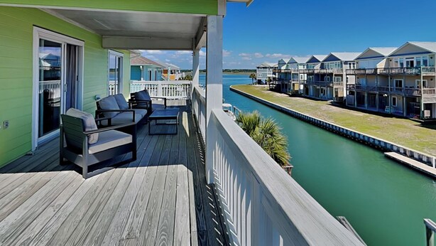 A waterfront property with a covered deck, outdoor furniture, and a canal view. - Driftwood | Canal Front, Sound View, Private Dock! (Topsail Beach)