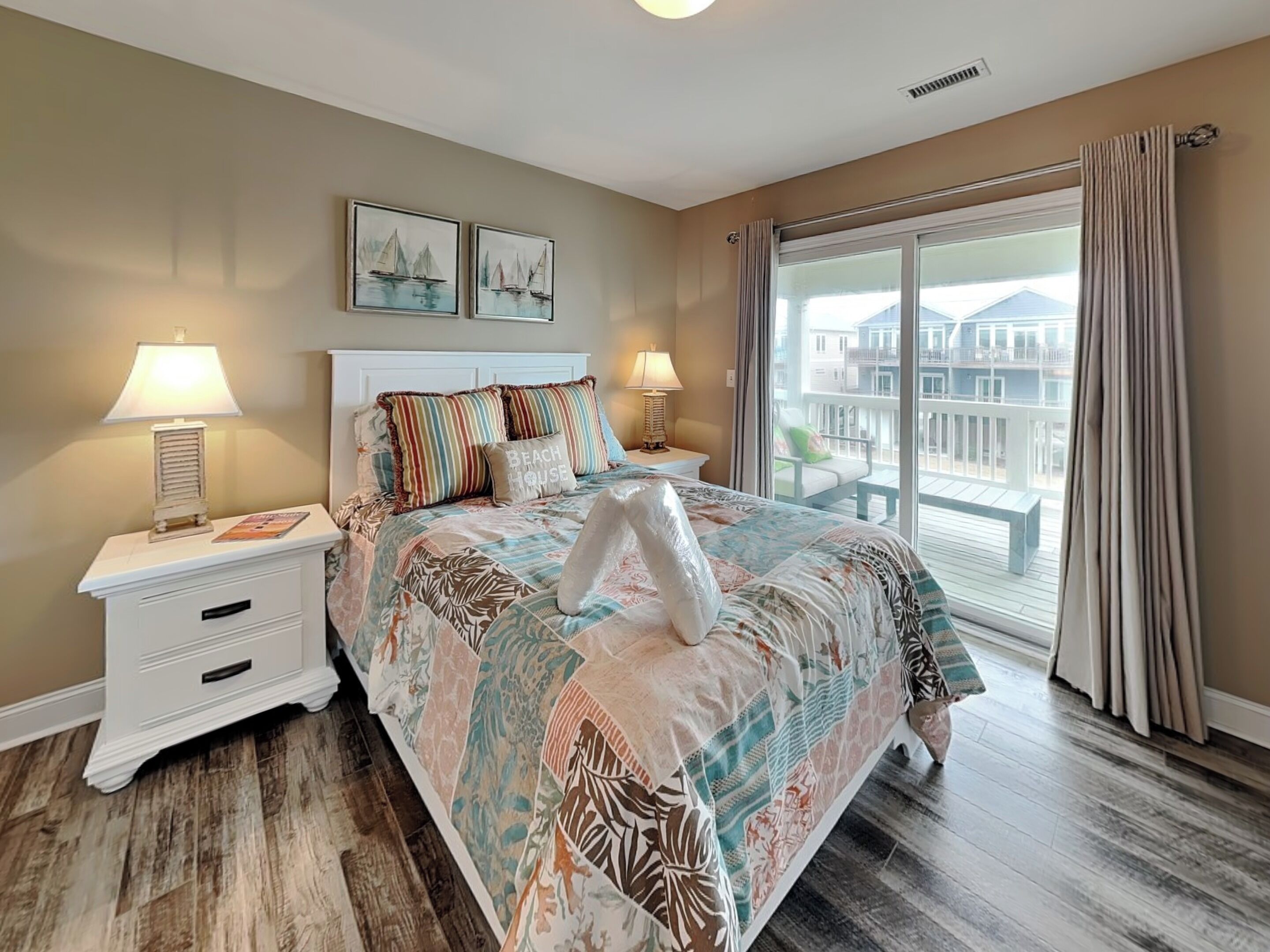 A bedroom with a large bed, two bedside tables, a nightstand, a window with curtains, and a balcony view.