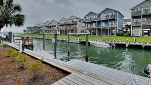 A waterfront property with multiple-story buildings, docks, and a small docked boat. - Driftwood | Canal Front, Sound View, Private Dock! (Topsail Beach)