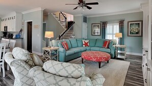 A living room with a teal sofa, patterned armchairs, a red ottoman, and a staircase leading to another level. - Driftwood | Canal Front, Sound View, Private Dock! (Topsail Beach)