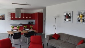 Un soggiorno moderno con un divano grigio, poltrone rosse e un'area pranzo con tavolo e sedie.