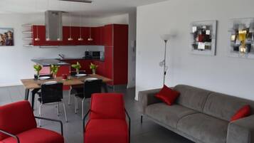 A modern living room with a grey sofa, red chairs, and a dining area with a table and chairs.