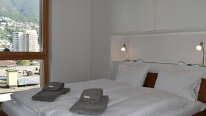 Un letto rifatto con lenzuola bianche e due asciugamani piegati, una testata in legno e due abat-jour.