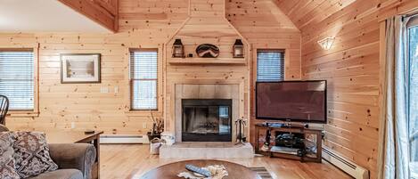 Un acogedor interior de cabaña de madera con chimenea, televisor y una zona de estar confortable.