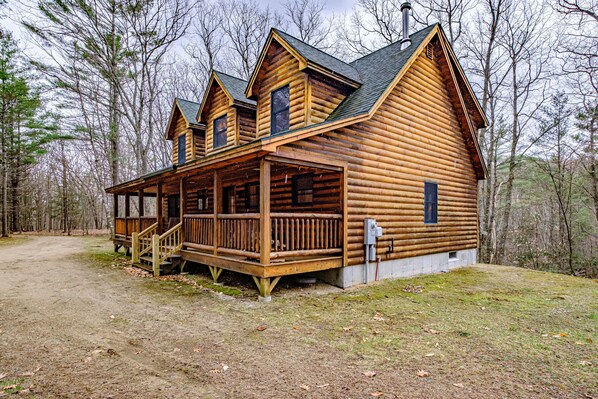 A log cabin with a porch and multiple windows, surrounded by trees.