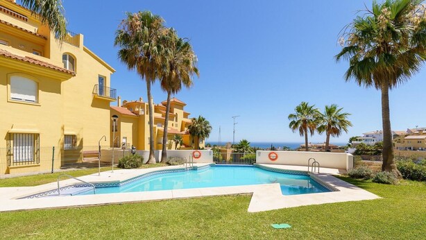 A swimming pool surrounded by well-maintained grass and palm trees, with a view of the sea and adjacent buildings. - Elegant Mijas Costa Holiday Home for 4 (Mijas Costa)