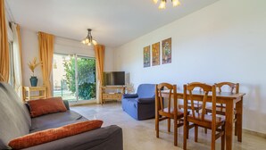 A living room with a sofa, a dining table with chairs, a TV, and a large window with curtains. - Elegant Mijas Costa Holiday Home for 4 (Mijas Costa)
