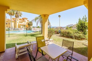 Un patio con mesa y sillas, piscina y vistas a edificios y palmeras.