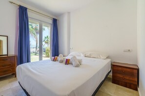 A hotel room with a bed, a wooden nightstand, a dresser, and a sliding glass door leading to a balcony.