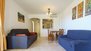 A living room with two sofas, a dining table with chairs, and a kitchen area visible through an archway. - Elegant Mijas Costa Holiday Home for 4 (Mijas Costa)