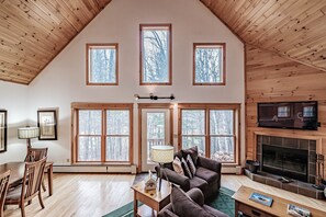Un salón amplio con techo alto, ventanas grandes, chimenea y televisor.