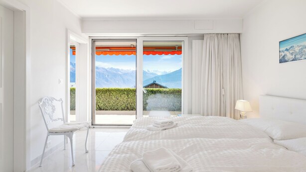 Habitación de hotel con una cama grande, una silla y vistas a la montaña a través de la puerta de vidrio.
