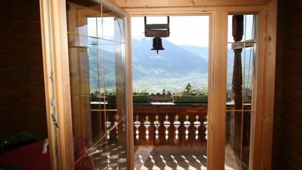 Una cabaña de madera con un ventanal de vidrio que da a un balcón con vistas a la montaña.