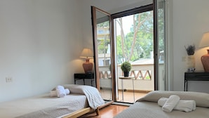 A hotel room with two beds, a small table with a lamp, a potted plant, and a view of the outside balcony. - Very cosy Townhouse 5 minutes walking to the beach  (Pals)