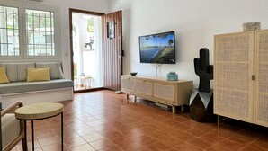 A living room with a TV, a sofa, a wooden cabinet, and a window with a view of the outdoors. - Very cosy Townhouse 5 minutes walking to the beach  (Pals)